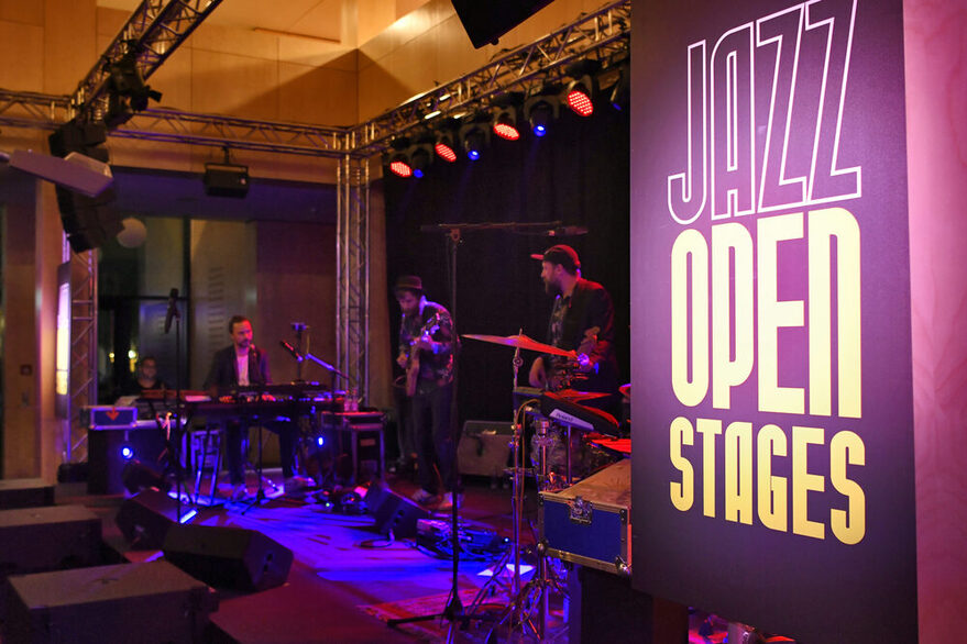 Bühne mit Musikern rechts ein lila Schild mit der Aufschrift: "Jazz Open Stages"