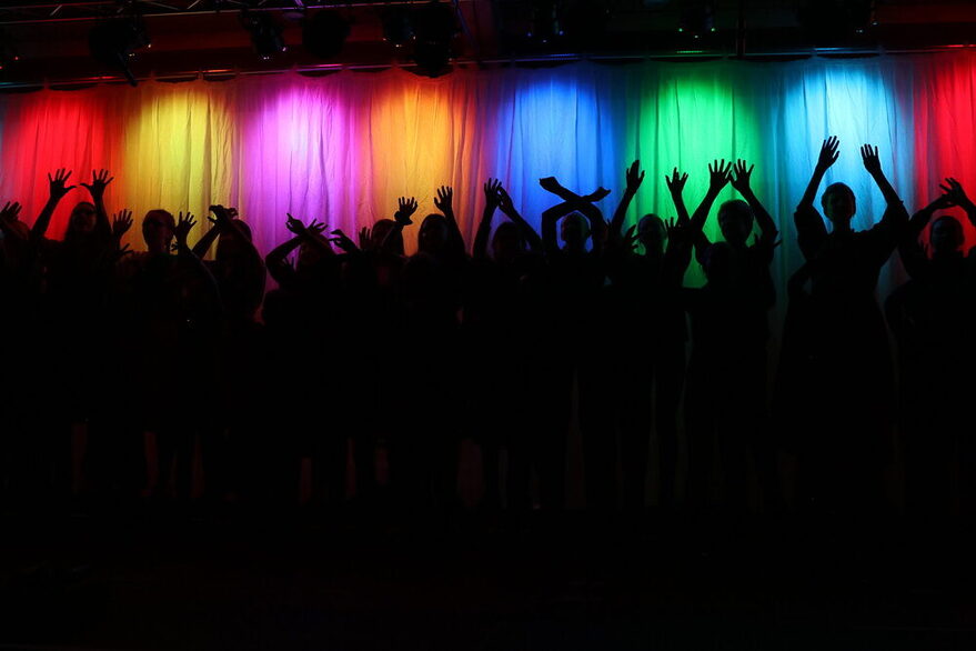 Kinder- und Jugendchor im Dunkeln auf der Bühne. Oben an der Bühne bunte Lichter