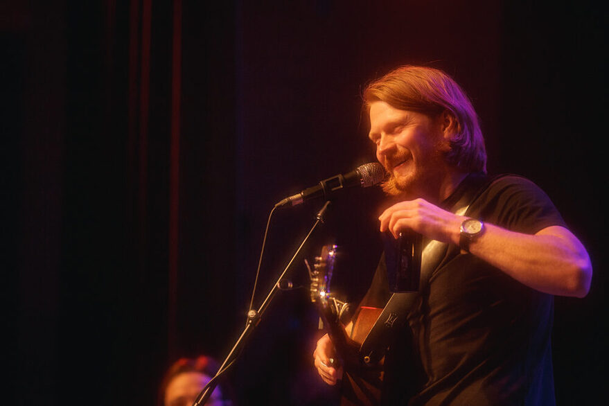 Ein Mann mit langen, braunen Haaren, Gitarre und Mikrofon