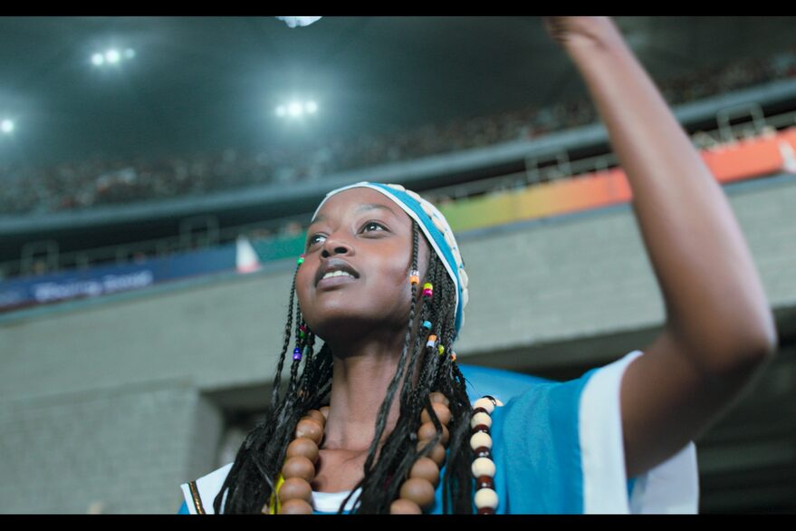 Afrikanische junge Frau im Stadion schaut nach oben und hält linken Arm nach oben (Siegerpose)