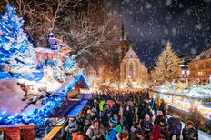 Top view in the dark of a decorated, illuminated Christmas market and buildings with passers-by in the snow.